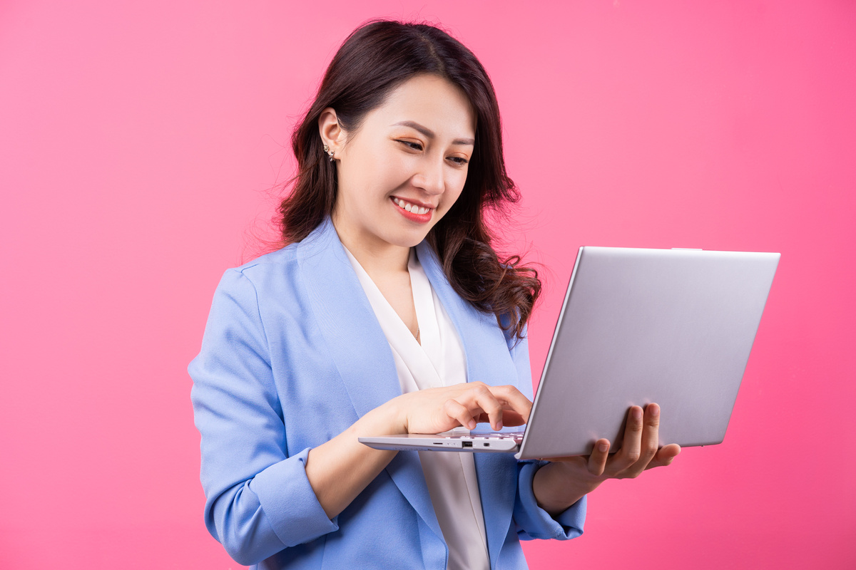 Asian Business Woman Holding Laptop on Pink Background