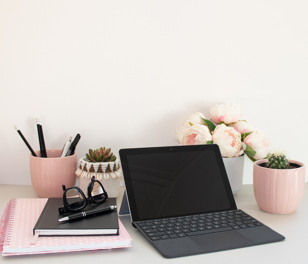 Home office laptop potted plants and pink notebook
